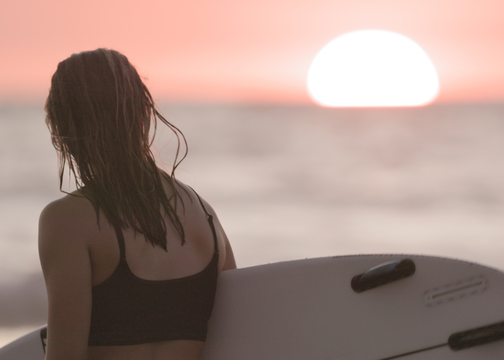 a pink Costa Rican sunset highlights a surfer holding her board