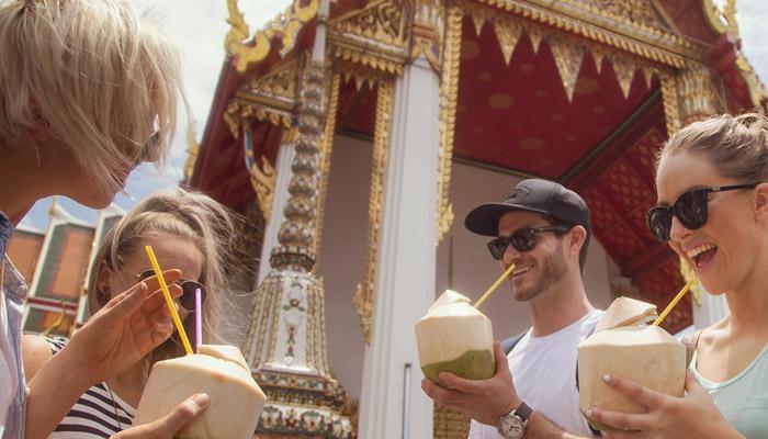 Four happy tourists drinking coconut water in Bangkok, Thailand