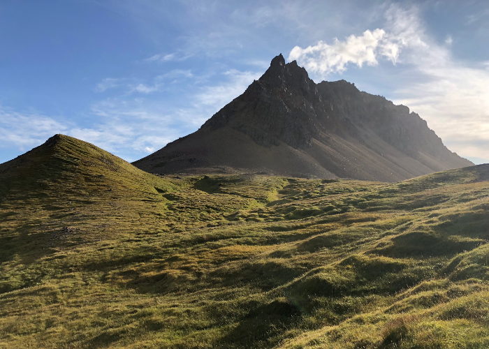 a jagged peak in the distance with the green mountains of Brúnavík pass in the foreground from a hike in Eastern Iceland